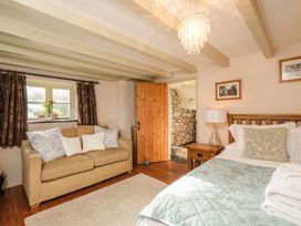 A bedroom with a bed pillow and blanket next to a wooden nightstand with a lamp and a beige sofa under a window at The Mill in Lostwithiel