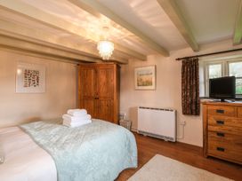 A bedroom with a bed covered by a quilt with folded towels on top a wooden wardrobe a dresser with a television and two framed pictures on the walls at The Mill in Lostwithiel