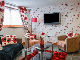 A living room with armchairs cushions and curtains featuring red floral patterns at Poppy Cottage in Aylesbeare