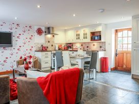 An open plan kitchen and living room with dining table and chairs red kitchen appliances and a wooden door at Poppy Cottage in Aylesbeare