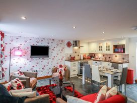 An open living room and kitchen with patterned wallpaper chairs dining table and kitchen appliances at Poppy Cottage in Aylesbeare