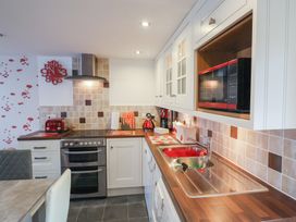 A kitchen with white cabinets red appliances and a stainless steel sink at Poppy Cottage in Aylesbeare