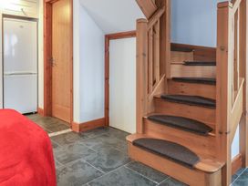 A wooden staircase with dark stair treads next to a white door and a refrigerator in a room with tiled floor at Poppy Cottage in Aylesbeare