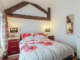 A bedroom with a double bed with floral bedding two bedside tables with lamps and a wall mirror at Poppy Cottage in Aylesbeare