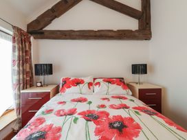 A bedroom with a bed that has red flower print bedding and two nightstands with lamps at Poppy Cottage in Aylesbeare