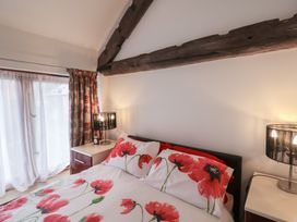A bedroom with a bed with red poppy bedding two bedside tables with lamps under a wooden beam at Poppy Cottage in Aylesbeare