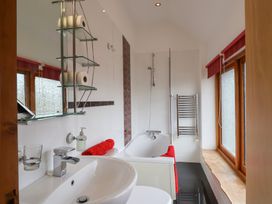 A bathroom with a sink a bathtub a glass shelf with toilet paper rolls and windows with red blinds at Poppy Cottage in Aylesbeare