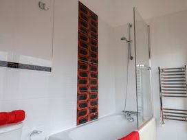 A bathroom with a bathtub shower combination red towels and patterned wall tiles at Poppy Cottage in Aylesbeare
