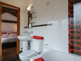 A bathroom with a toilet sink and bathtub with red towels and a bedroom visible through an open door at Poppy Cottage in Aylesbeare