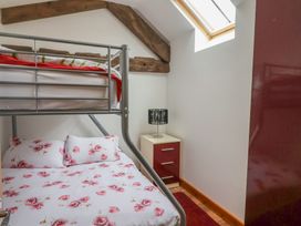 A bedroom with a metal bunk bed with floral bedding a bedside table with a lamp and a skylight at Poppy Cottage in Aylesbeare