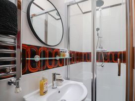A bathroom with a sink a round mirror towel rack and a shower with glass door at Poppy Cottage in Aylesbeare