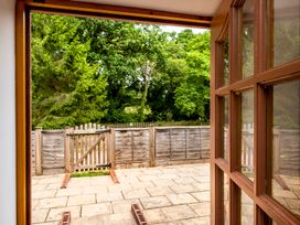 A view through an open wooden door showing a paved patio area a wooden fence and gate with trees in the background at Poppy Cottage in Aylesbeare
