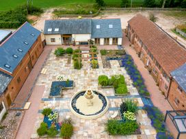 A courtyard with a circular fountain in the center surrounded by flower beds and pathways between brick buildings at Poppy Cottage in Aylesbeare