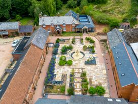 Aerial view of a courtyard with a central water fountain surrounded by garden beds and three brick buildings at Poppy Cottage in Aylesbeare