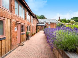 A brick paved pathway between red brick buildings with potted plants and purple flowers at Poppy Cottage in Aylesbeare