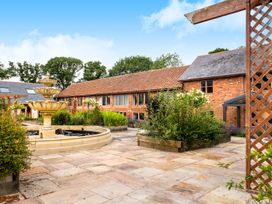 A courtyard with a tiered fountain surrounded by plants and brick buildings at Poppy Cottage in Aylesbeare