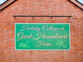 A green sign on a brick building wall reading Holiday Cottages at Great Houndbeare Farm