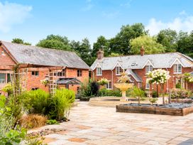 A courtyard with a stone fountain and flower beds in front of red brick buildings at Poppy Cottage in Aylesbeare