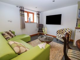 A living room with a green sofa a round glass coffee table a wall mounted TV and two chairs at Lime Cottage in Aylesbeare
