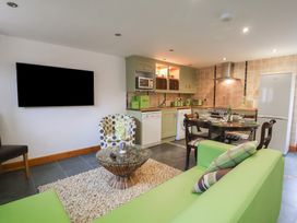 An open plan room with a green sofa, a round wooden dining table with chairs, a kitchen area with appliances, and a wall-mounted TV at Lime Cottage in Aylesbeare