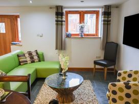 A living room with a green sectional sofa a glass coffee table on a textured rug a polka dot armchair a black chair and wooden framed windows at Lime Cottage in Aylesbeare