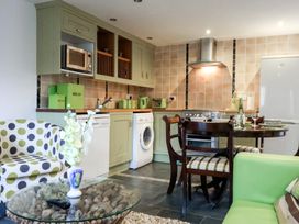 A kitchen with green cabinets and appliances next to a dining table with chairs and a glass coffee table at Lime Cottage in Aylesbeare
