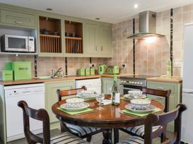A kitchen with a round wooden dining table set for four and green kitchen cabinets at Lime Cottage in Aylesbeare