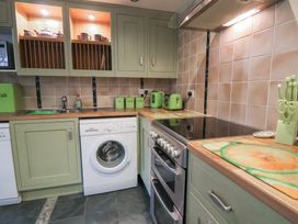 A kitchen with green cabinets a washing machine a stove a sink and kitchen utensils at Lime Cottage in Aylesbeare