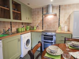 A kitchen with green cabinets appliances and a dining table set with dishes and glasses at Lime Cottage in Aylesbeare