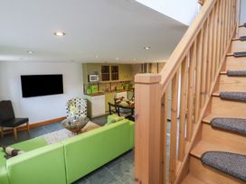 A living area with green sofa TV wooden staircase and kitchen at Lime Cottage in Aylesbeare