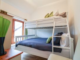 A bedroom with a white bunk bed with dark and light bedding and pillows next to a wooden window at Lime Cottage in Aylesbeare