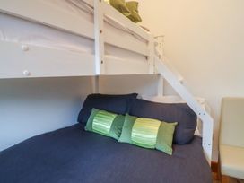A bunk bed with green pillows and navy bedding next to a beige chair at Lime Cottage in Aylesbeare