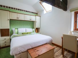 A bedroom with a bed flanked by cupboards and a window with a desk and chair at Lime Cottage in Aylesbeare