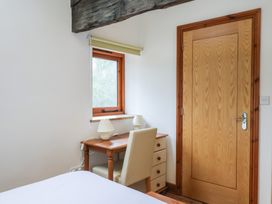 A small wooden desk with two lamps and a chair next to a window and a wooden door in a bedroom at Lime Cottage in Aylesbeare