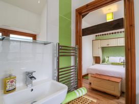 A bathroom sink with soap and towel and a view into a bedroom with bed chest and overhead cabinets at Lime Cottage in Aylesbeare
