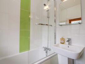 A bathroom with a bathtub shower combination and a sink with a mirror and soap at Lime Cottage in Aylesbeare