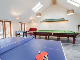 A game room with a ping pong table with paddles and ball a pool table foosball table and red armchair at Lime Cottage in Aylesbeare