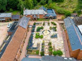 An aerial view of a property with multiple brick buildings surrounding a central courtyard with a stone fountain and planted garden beds at Lime Cottage in Aylesbeare