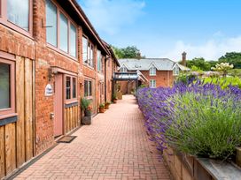 A pathway with potted plants along a brick building and lavender plants on the right at Lime Cottage in Aylesbeare