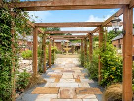 A pathway with wooden trellis and plants leading to a fountain in front of brick buildings at Lime Cottage in Aylesbeare