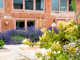 Yellow flowers and purple plants outside a brick house with stone pavement at Lime Cottage in Aylesbeare