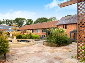 An outdoor courtyard with a stone fountain raised flower beds and a brick building with tiled roofs at Lime Cottage in Aylesbeare