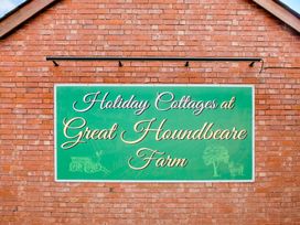 A green sign on a red brick wall with text holiday cottages at Great Houndbeare Farm