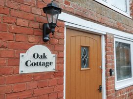 The outside wall of a brick house with a wooden door a black lantern and a sign saying Oak Cottage at Oak Cottage in Aylesbeare