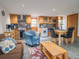 An open kitchen and living area with wooden cabinets a blue armchair a brown sofa and a dining table at Oak Cottage in Aylesbeare