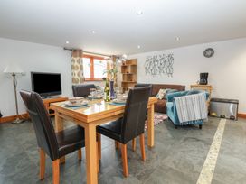A dining and living area with a wooden table set for four and a television in Oak Cottage Aylesbeare