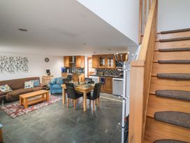 An open plan living room and kitchen with a dining table four chairs a brown sofa an armchair and wooden stairs at Oak Cottage in Aylesbeare