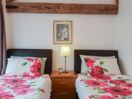 A bedroom with two single beds with floral bedding a bedside table with a lamp and alarm clock and a framed picture on the wall at Oak Cottage in Aylesbeare