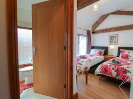 A bedroom with two single beds with floral bedding and a bathroom with a toilet and wooden door at Oak Cottage in Aylesbeare