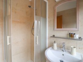 A bathroom with a shower enclosure a sink with a soap dispenser and cup and a mirror above the sink at Oak Cottage in Aylesbeare